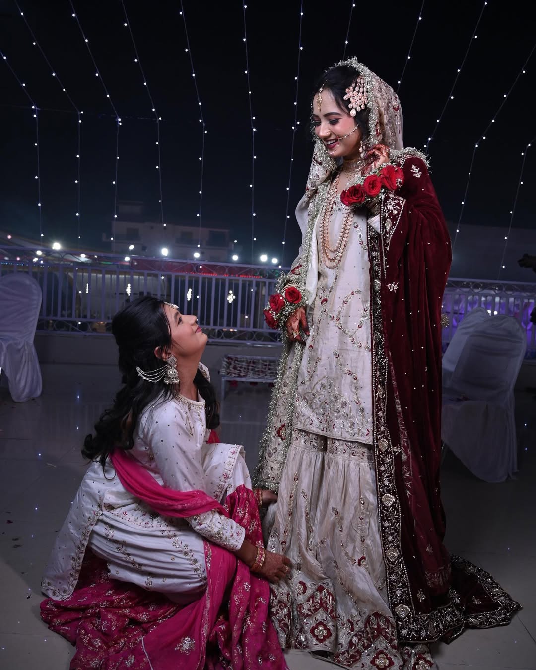 Two women in traditional attire standing under a starry sky with decorative lights.