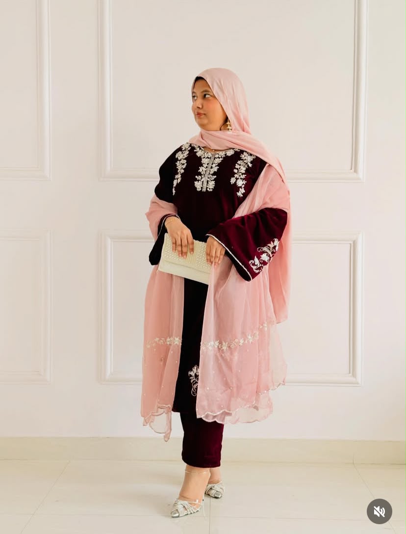 A woman models a traditional South Asian outfit featuring a dusty pink dupatta and a matching pink tunic with deep maroon velvet sleeves and silver floral embroidery, paired with maroon pants and a light pink hijab.